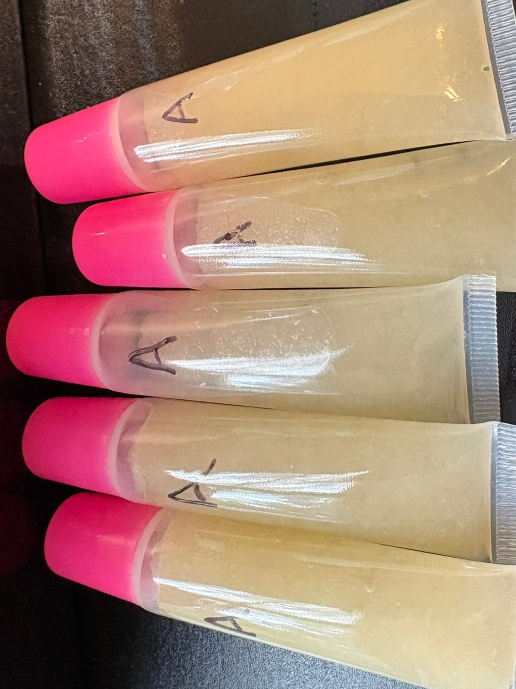 Five tubes of cream with pink caps on a dark surface